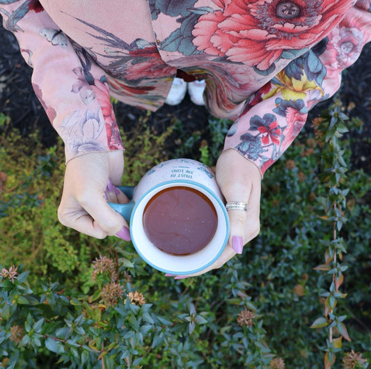 Top-down view of a cup of tea, hands, shoes, and a floral jacket.
