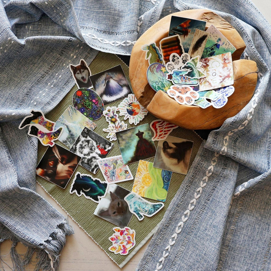 Collection of SLChristley Designs nature, music, and animal inspired stickers displayed in a wooden bowl with light blue and light green fabric.