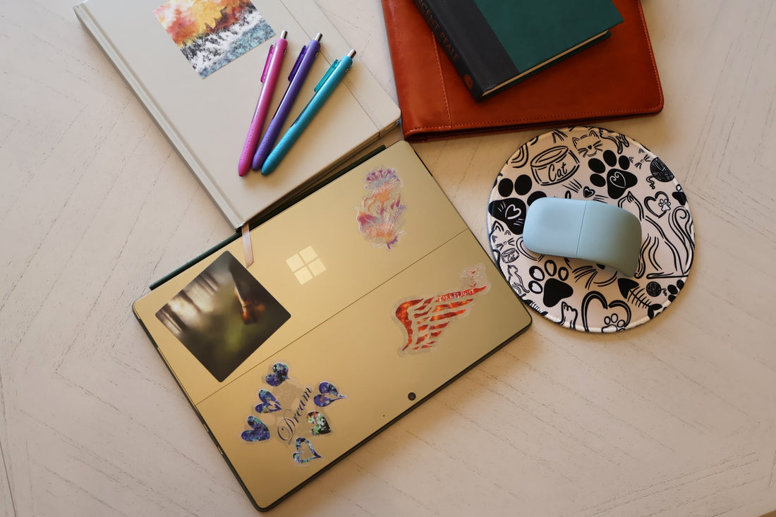 Journals, pens, SLChristley Designs Feline Fables mousepad, and laptop styled with music, quote, and nature-inspired stickers on a table.